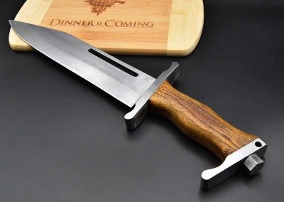 Dies ist ein Foto eines hangemachten Jagdmessers der Messerschmiede Jettenbach. Dieses liegt auf einem Holzbrett im Game of Thrones Stil.